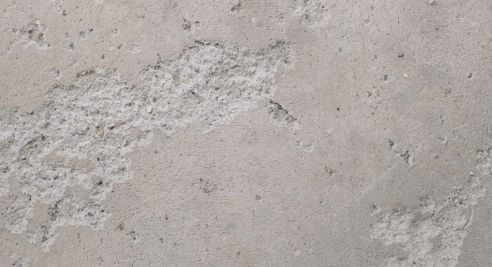 The image show an example of spalling and scaling on concrete. This type of damage is caused by the freeze thaw cycle. The photo shows a wall of concrete with several small holes and irregular missing parts. The wall should have been smooth and complete. 