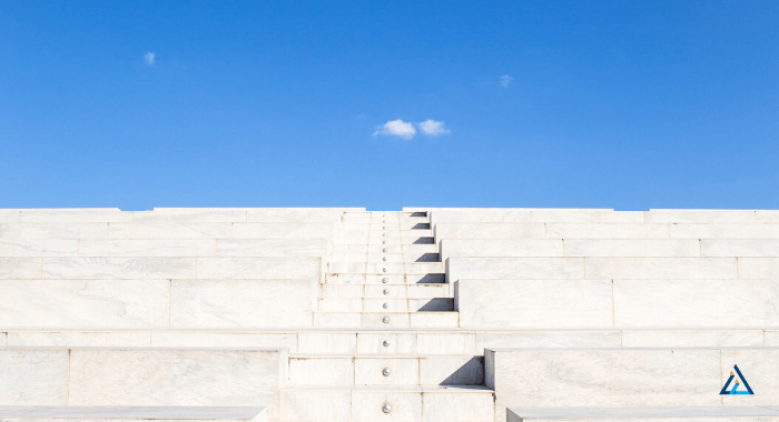 Image is a photo of concrete stairs taken from below. The angle leads the eye to to the top of the stairs. The concrete stairs are light gray and contrast with the clear blue sky on the horizon. The stairs do not look new, but in excelent shape. Most likely air entrained concrete was used to make them last the outdoor conditions.