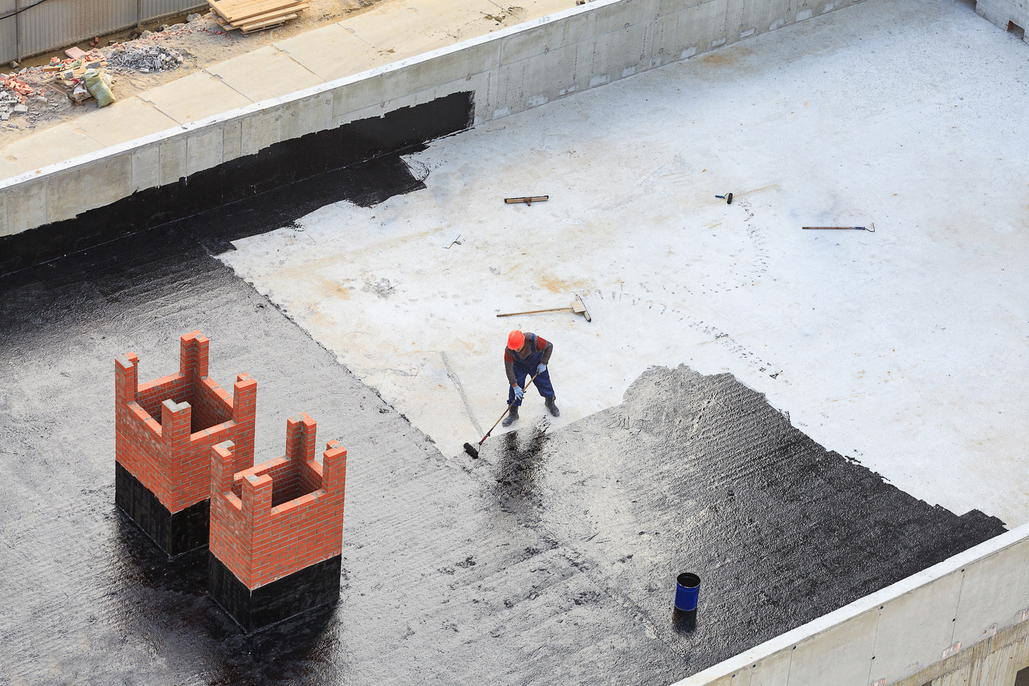 Workers conduct waterproofing of the roof with bitumen.